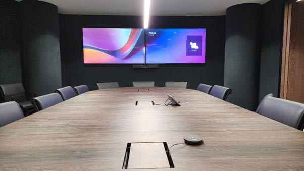 Boardroom setup showing dual screen, with control surface and expansion microphone on the table